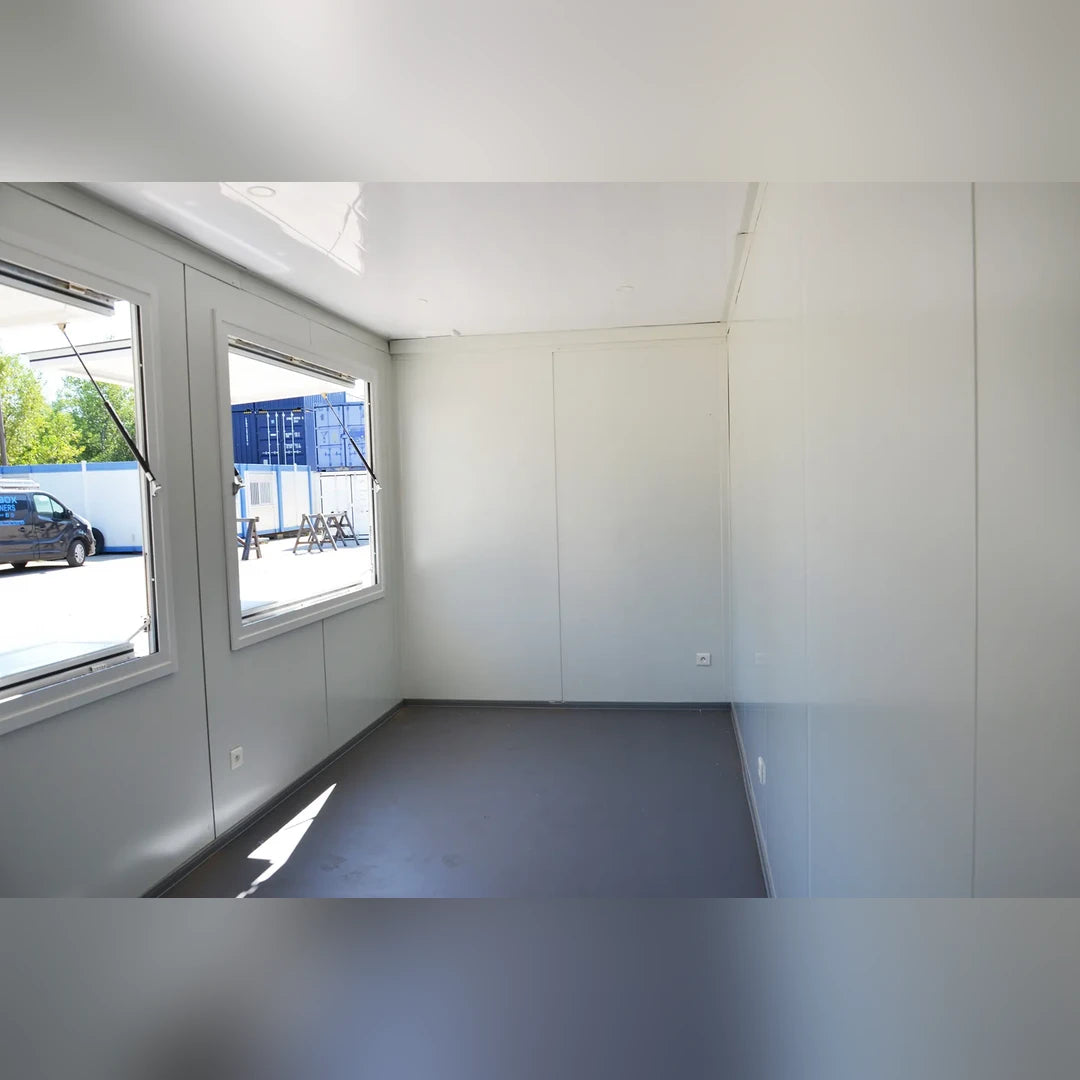 Intérieur bungalow modulaire Eurocontex – grande fenêtre ouvrant avec lumière naturelle, murs blancs et sol gris